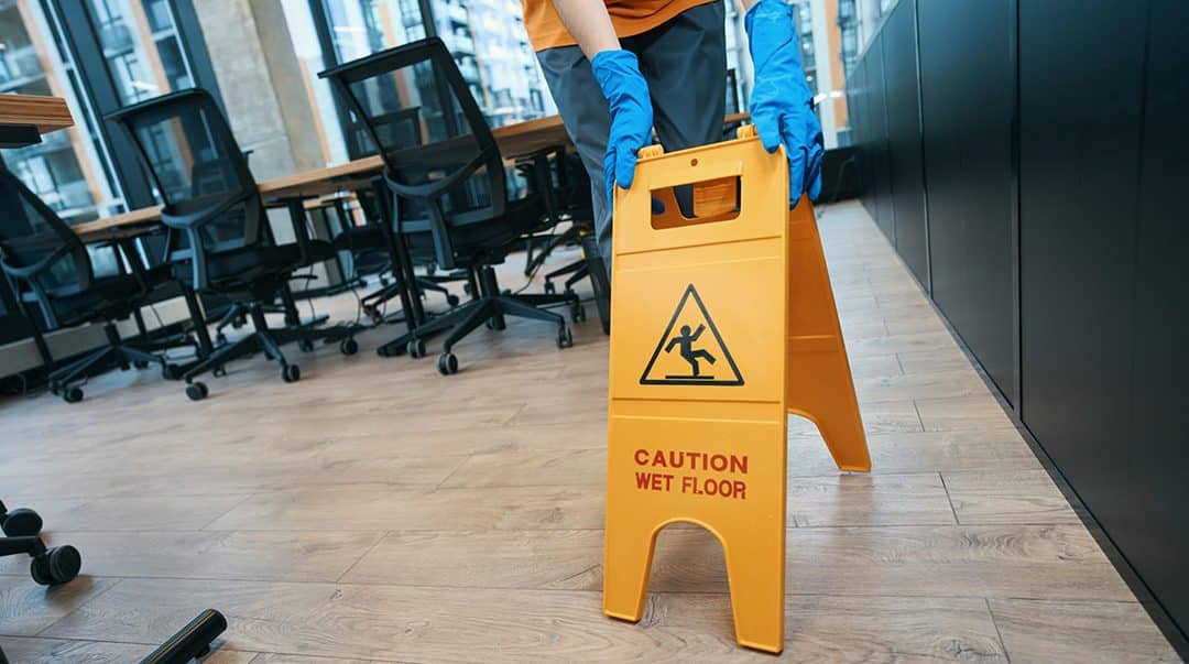 Janitor in an office posting a wet floor caution sign